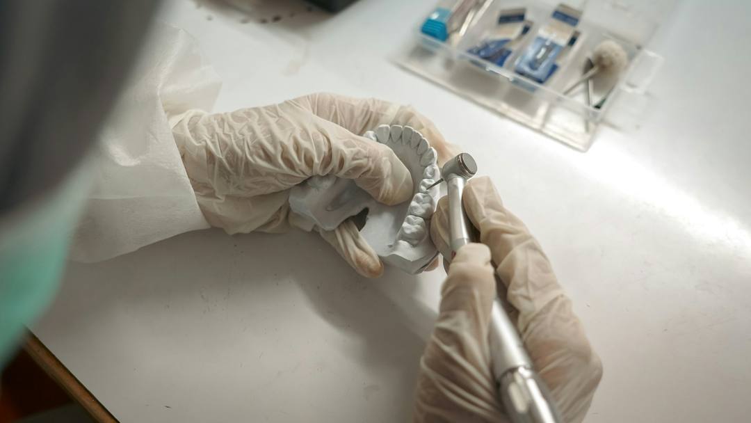 Mani guantate lavorano un modello in gesso col manipolo