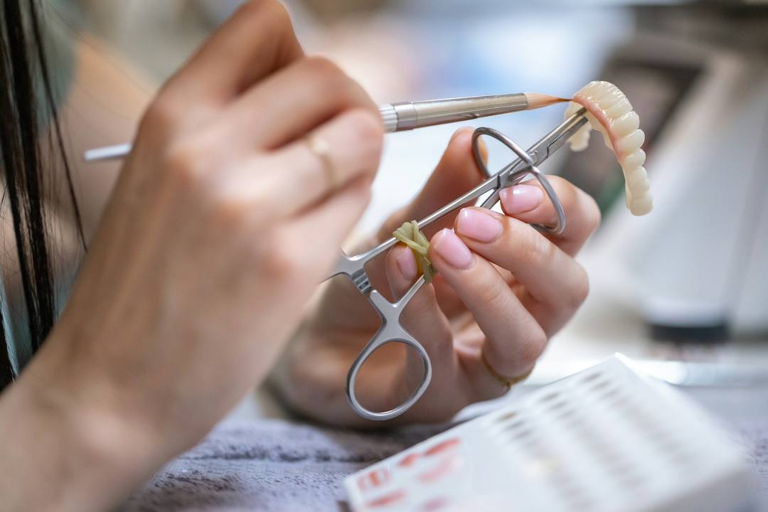 Una mano col pennello rifinisce un’arcata completa tenuta con la pinza
