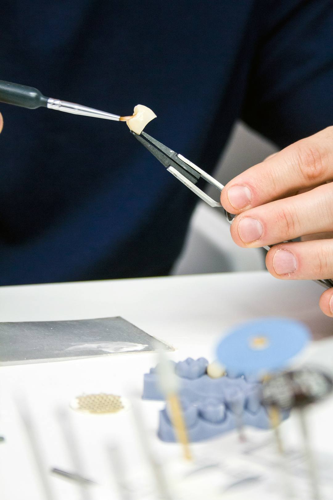 Un pennello deposita la ceramica su un dente tenuto con la pinzetta