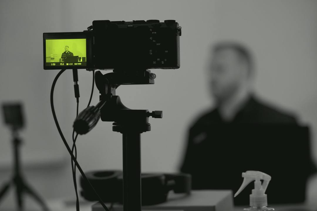 Una fotocamera su treppiede riprende il relatore; sul monitor l'immagine è accesa in lime